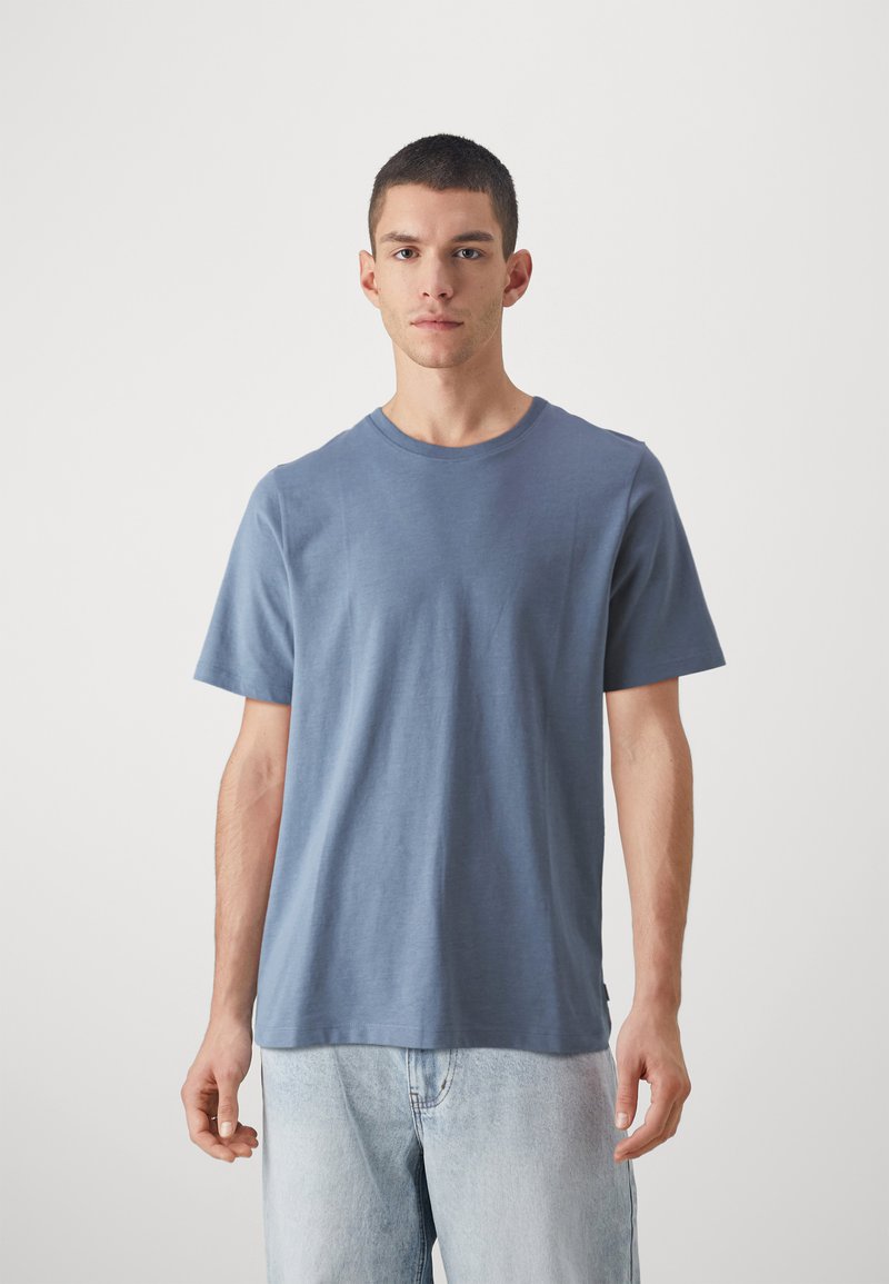 Blå bomullen t-shirt med kort ärm, rund halsringning, slät textur och avslappnad passform. Bärs med ljus tvättade denimshorts.