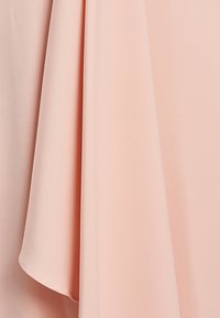 Textília v broskyňovej farbe s hladkou, jemnou textúrou, elegantne sa splývajúca s jemným leskom. Má prúdiace záhyby s čistými okrajmi.