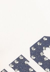 Close-up van marineblauwe glinsterende stofpatches met zilveren ronde studs, gerangschikt op een witte, gestructureerde achtergrond.