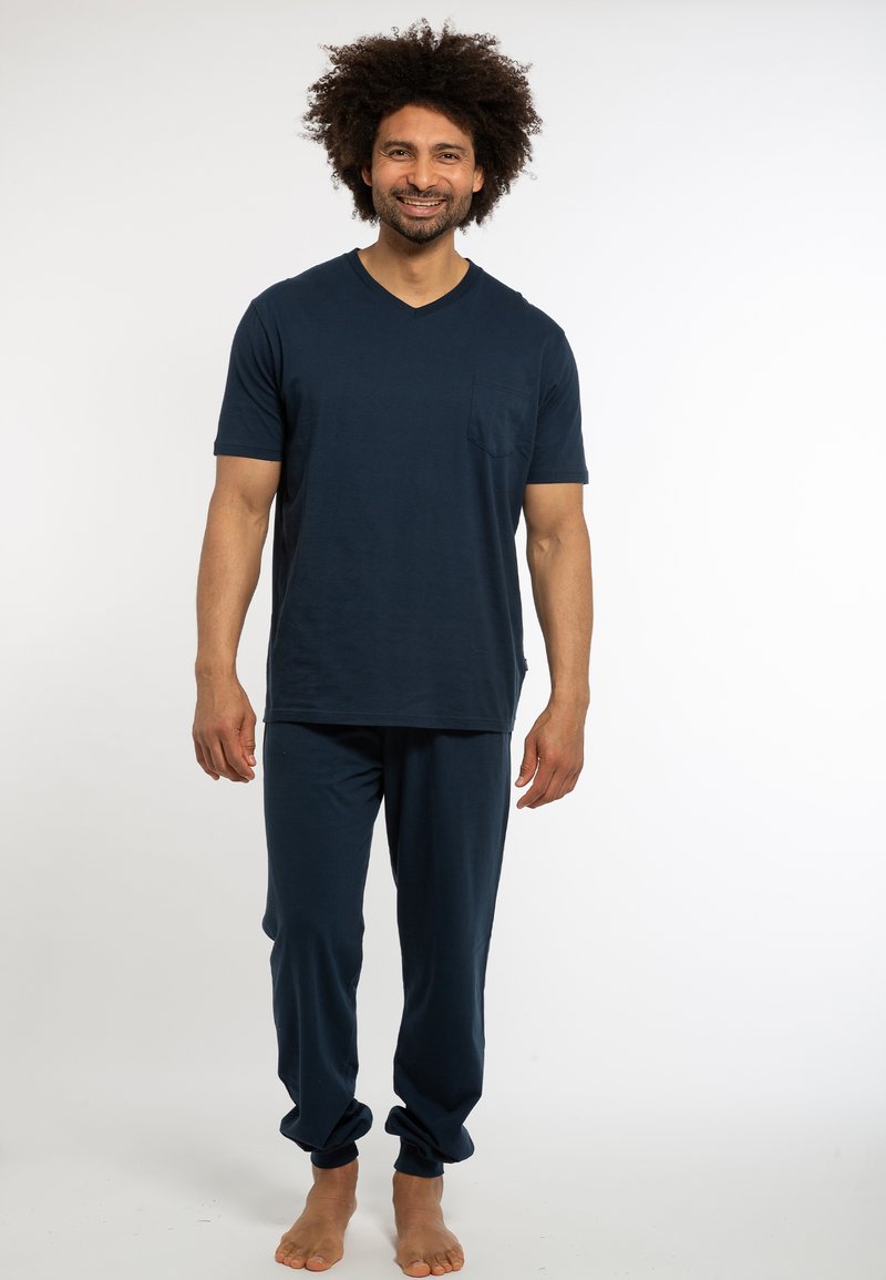 Completo loungewear blu navy realizzato in tessuto morbido; maglietta a maniche corte con scollo a V e taschino sul petto, abbinata a pantaloni larghi e tapered.