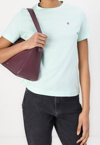 Lys mintgrøn t-shirt med logo, korte ærmer, parret med en triangelformet bordeaux håndtaske og sorte denim jeans. Glat bomuldsstruktur.