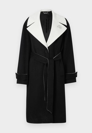Manteau en laine noir avec un large col blanc, taille ceinturée, boutons à l'avant et surpiqûres blanches contrastées aux poignets et à l'ourlet.