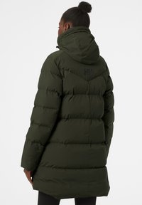 Donkergroene pufferjas met een capuchon, met een quilted ontwerp en een logo op de achterkant. Het materiaal lijkt lichtgewicht maar tegelijkertijd isolerend te zijn.