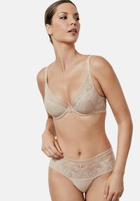 Ensemble de lingerie en dentelle beige avec soutien-gorge et culotte assortis, présentant des motifs floraux, des bretelles ajustables et un subtil accent doré sur la taille.