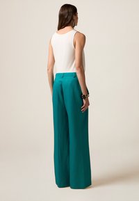 Weite teal-farbene Hosen mit glatter Textur und tailliertem Schnitt, kombiniert mit einem enganliegenden weißen Tanktop. Einfaches Design, keine sichtbaren Muster.