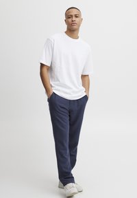 Tricou alb din bumbac, combinat cu pantaloni din in bleumarin, cu o croială relaxată, prevăzuți cu buzunare laterale, completat cu adidași albi. Design minimalist.