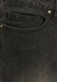 Sort denimstof har en fremtrædende lomme med sølvhardware. Teksturen er glat med en let glans og et klassisk fit design.