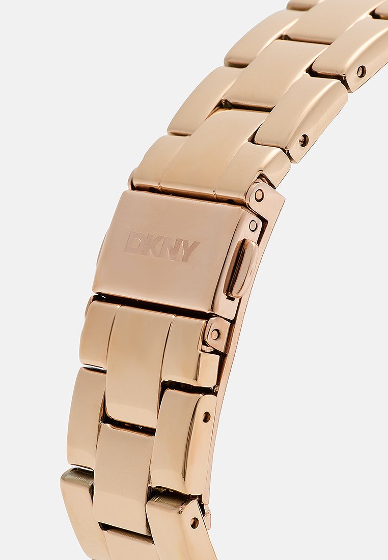 Reloj de metal con pulsera de tono dorado rosa pulido. Presenta eslabones entrelazados y un cierre con el logo grabado 'DKNY'.