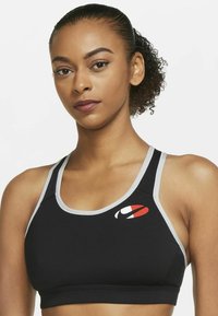 Reggiseno sportivo nero con dettagli grigi, con un logo sul lato sinistro. Il tessuto sembra elastico e aderente, progettato per le prestazioni.