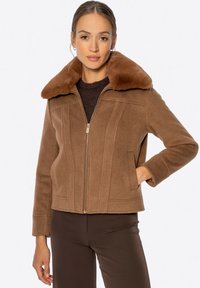 Braune Schaffelljacke mit großem, weichem Kragen, Frontreißverschluss und vertikalen Nähten. Verfügt über Seitentaschen und lange Ärmel.