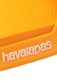 Suola in gomma arancione brillante con superficie testurizzata. Logo Havaianas in bianco ben visibile sul lato. Design semplice e piatto.