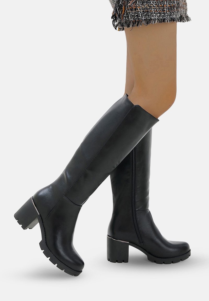 Las botas negras hasta la rodilla están hechas de un material sintético liso, cuentan con un tacón grueso, punta redondeada y una cremallera lateral para ponérselas fácilmente. Suela texturizada para mayor agarre.