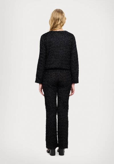 Černý texturovaný outfit z huňatého materiálu, s volně střiženým topem a úzkými kalhotami. Design má zkrácenou délku a rozšířené lemy.
