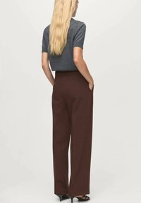 Top gris de manga corta con un acabado texturizado, combinado con pantalones marrones de pierna ancha y cintura alta con bolsillos laterales, mostrados desde atrás.