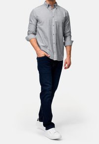 Szara koszula z długim rękawem, z kieszenią, z podwiniętymi rękawami, w zestawieniu z ciemnymi dżinsami i białymi trampkami. Prosty design i przewiewny materiał.