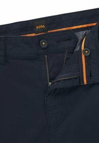 Navy broek met een rits en knoopsluiting. Voorzien van oranje accentstiksels en een gestructureerde binnenvoering. Merkenlabel "BOSS" op de tailleband.