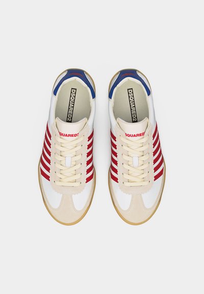 Λευκά αθλητικά παπούτσια με κόκκινες ρίγες, μπεζ κάπες στα δάχτυλα, μπλε λεπτομέρειες στη φτέρνα και λογότυπο "DSQUARED2" στη γλώσσα και στην εσωτερική σόλα, φαίνονται από πάνω.