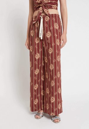 Donna che indossa pantaloni ampi color granata con motivo floreale e a righe, abbinati a sandali argento open toe e un top corto annodato coordinato.