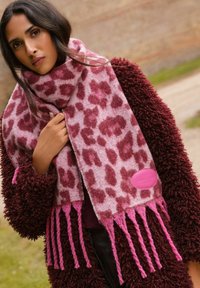 Bufanda de estampado de leopardo en suave rosa y burdeos con extremos con flecos y un acabado texturizado, combinada con un abrigo borroso en color burdeos.