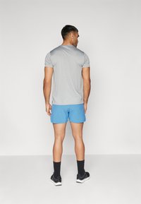Camiseta atlética cinza de mangas curtas combinada com calções atléticos azuis, meias de tornozelo pretas e ténis pretos. Design simples, sem padrões.