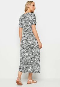 Schwarz-weiß gemustertes Maxikleid mit kurzen Ärmeln, tailliertem Schnitt und fließendem Rock. Das Modell trägt flache Sandalen.