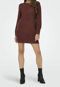 Abito a maglia bordeaux con maniche lunghe, scollo tondo e texture a coste. Abbinato a stivaletti neri con tacco, che mettono in risalto una silhouette aderente.