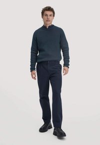 Donkerblauwe geribde trui met hoge kraag, gecombineerd met marineblauwe broek en zwarte chunkyschoenen. Model staat tegen een effen achtergrond.