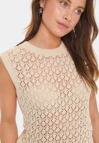 Top tricotat fără mâneci, de culoare bej, cu un model de dantelă florală și decolteu cu nervuri. Design ușor, cu țesătură deschisă, care sporește respirabilitatea.