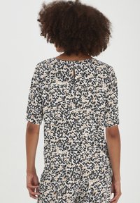 Blusa a maniche corte con stampa animale nei colori nero, bianco e beige, caratterizzata da un dettaglio a chiave sulla parte posteriore e una vestibilità rilassata.