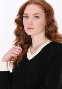 Pulover negru cu textură ribbed, de tip V, și accente de culoare crem la guler și manșete. Purtaț de un model cu păr ondulat roșu.