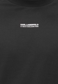 Juodas medvilninis džemperis su aukšta apykakle ir baltu užrašu ant krūtinės: „KARL LAGERFELD 21 RUE ST-GUILLAUME PARIS".