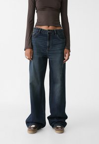 Tmavě modré široké džíny s opraným vzhledem, designem s pěti kapsami, prošitými detaily a knoflíkovým zapínáním v pase.
