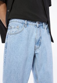 Jeans din denim de un albastru deschis, cu o croială relaxată, cusături vizibile, două buzunare frontale și închidere cu nasture la talie.