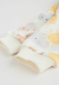 Pamut pulóver bordázott mandzsettával, színes állat- és napmintákkal egy puha krémszínű háttéren. Pasztell színű díszítések.