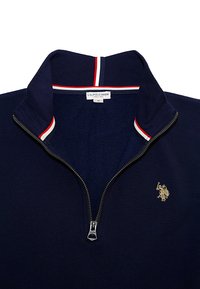 Navy pullover with a zip collar, featuring red and white striped accents and a gold embroidered logo on the left side. Soft texture.