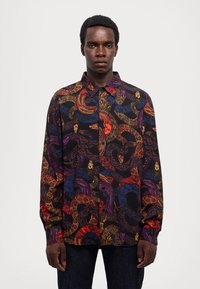 Camicia nera con bottoni caratterizzata da un motivo colorato e intricato di serpenti e volti nei toni del rosso, viola e oro. Maniche lunghe, vestibilità comoda.