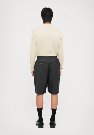 Helles beige Langarmhemd und dunkelgraue Shorts mit lockerer Passform. Die Shorts verfügen über Gesäßtaschen und einen elastischen Bund. Schwarze Socken und Schuhe.