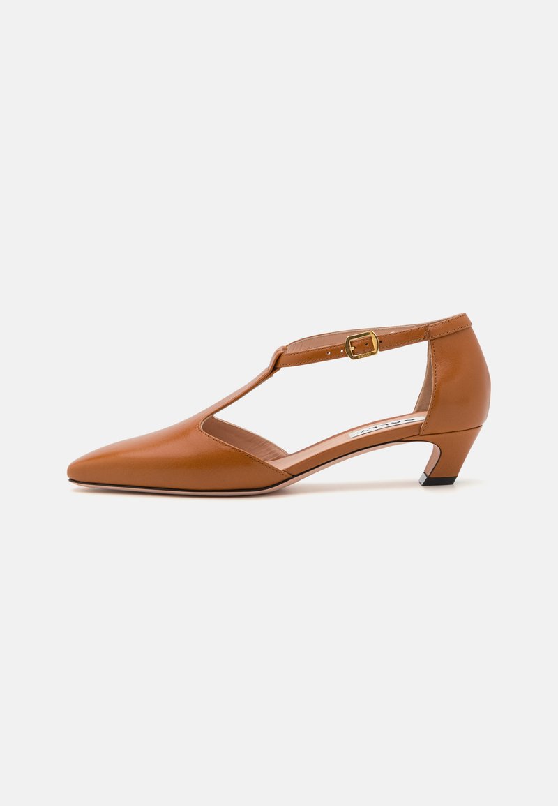 Brown leather high-heel shoe with a pointed toe, T-strap design, adjustable buckle, and a low angled heel. Smooth texture and sleek finish.