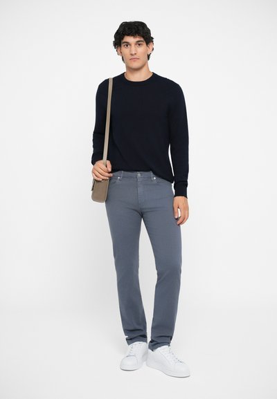 Marine Crewneck-Pullover, hellgraue Slim-Fit-Jeans, weiße Sneakers und beiger Umhängetasche. Glattes Material, minimalistisches Design, schlichte Hardware.