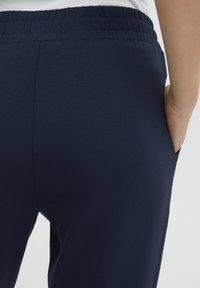 Mörkblå byxor med elastisk midja och en slät yta, utrustade med sidofickor och en enkel, strömlinjeformad design.