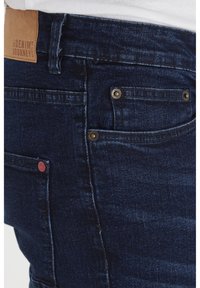 Mörkblå denimjeans med en läderetikett på midjan, guldfärgad hårdvara och en minimalistisk design med standardfickplaceringar.