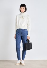 Hvit kort genser med høy hals og "CK"-logo, blå jeans, hvite plattform sneakers og liten svart veske.