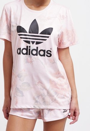 Roze Adidas T-shirt met bloemenpatroon, een zwart logo en drie strepen; gecombineerd met roze shorts met een klein logo aan de zoom.