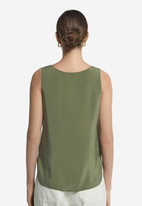 Top senza maniche verde oliva con una texture liscia, scollatura rotonda e orlo curvo, abbinato a pantaloni di colore chiaro.