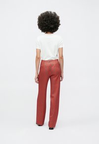 Hvid kortærmet skjorte kombineret med højtaljede røde bukser med mønster og geometrisk design. Glat stof, vidde ben, sorte sko.