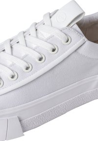 Białe płócienne trampki z okrągłym noskiem, sznurowadłem i teksturowaną gumową podeszwą. Posiadają metalowe oczka oraz małą metkę z logo na pięcie.