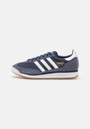 Granatowy sneaker Adidas SL 72 z białymi paskami, zamszowymi nakładkami, gumową podeszwą i markowym logo na boku i pięcie.