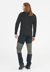 Sort langærmet skjorte parret med navy og olivengrønne bukser med en lynlåslomme og tekstureret stof. Båret med sorte vandrestøvler.