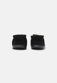 Black slippers with a soft, textured upper and low profile. Features a cushioned sole and a fold-over cuff for comfort and ease.