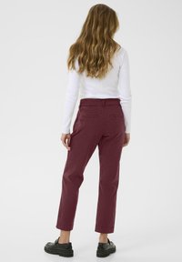 Burgundy cotton pants with a straight leg, featuring a mid-rise waist and back pockets, paired with black platform shoes.